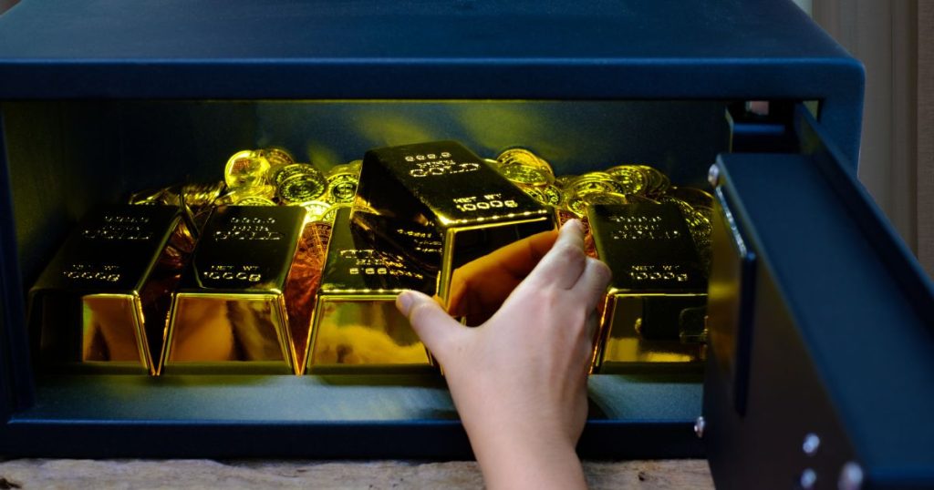 A hand retrieves gold bars from a safe.